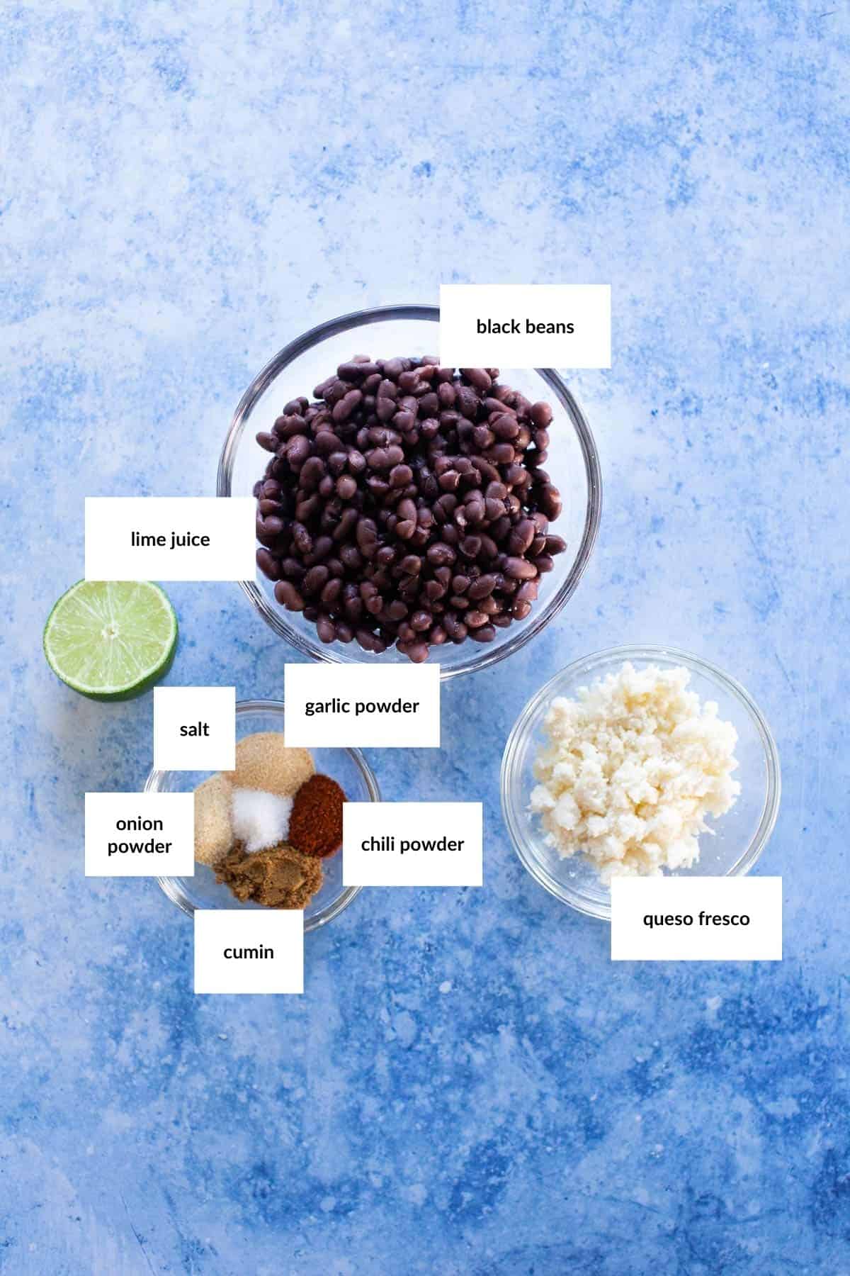 Three bowls with labeled ingredients: black beans, queso fresco, and spices (garlic powder, chili powder, onion powder, cumin, salt), plus a halved lime for lime juice.