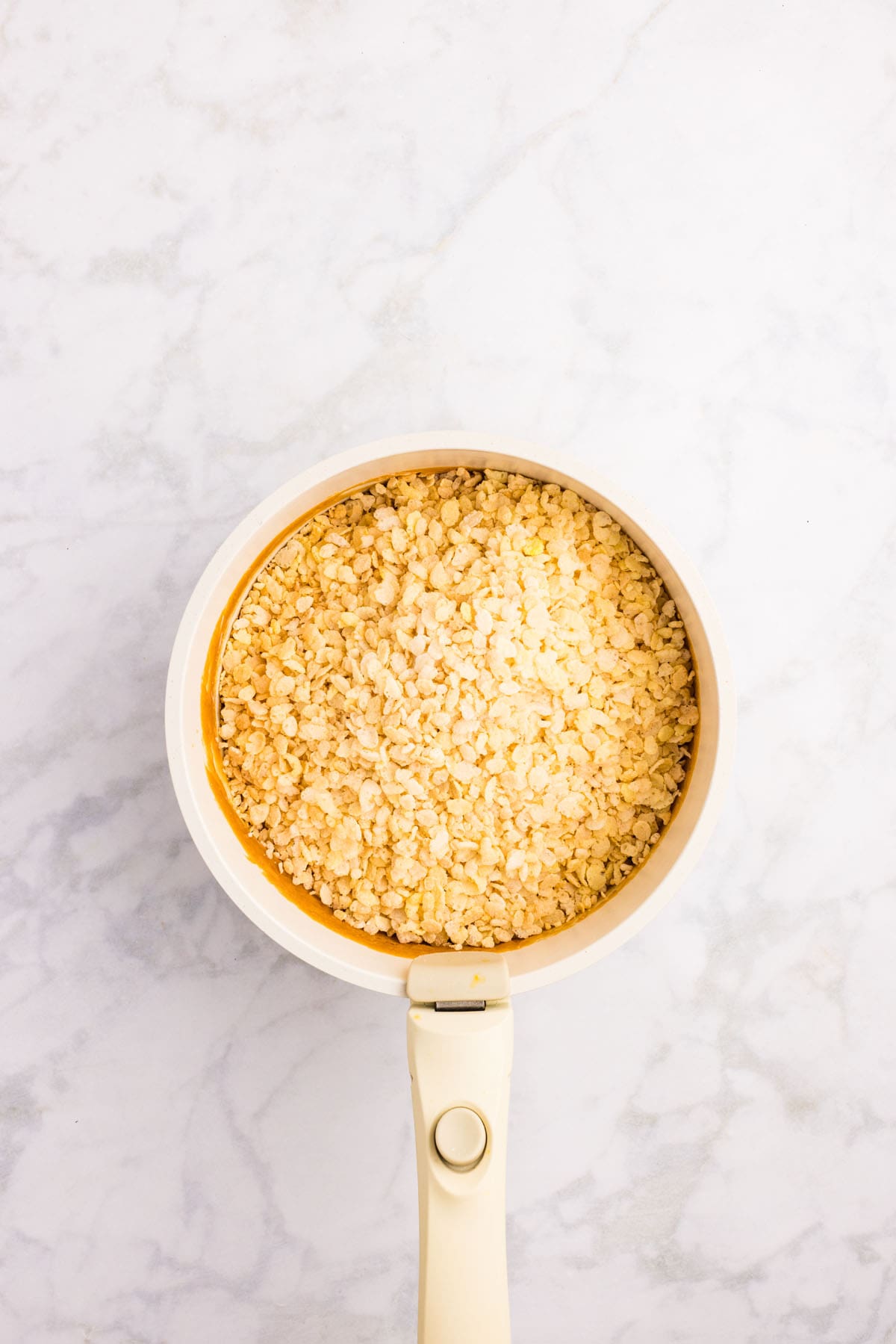 A white saucepan filled with uncooked rolled oats sits on a light marble countertop.