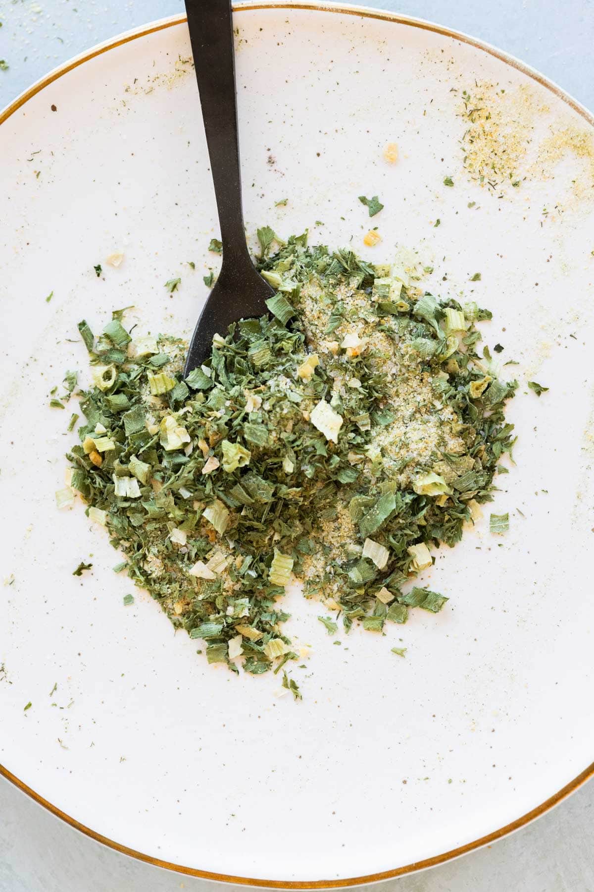 A white plate with a mixture of ranch seasoning, stirred with a black spoon.