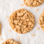 Five oatmeal cookies on parchment paper with scattered oats.