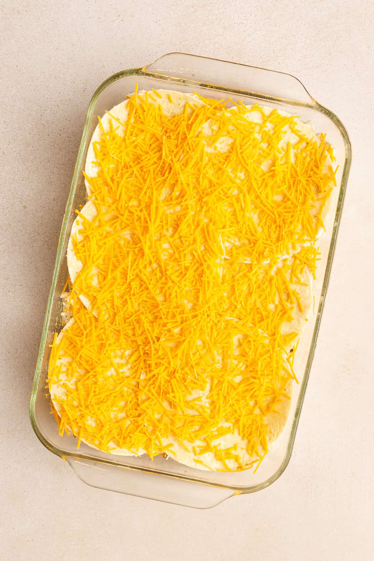 A glass baking dish filled with a layered casserole topped with a generous amount of shredded yellow cheese.