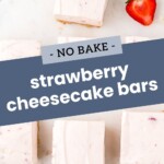 Squares of no-bake strawberry cheesecake bars arranged on a white surface with fresh strawberries nearby.