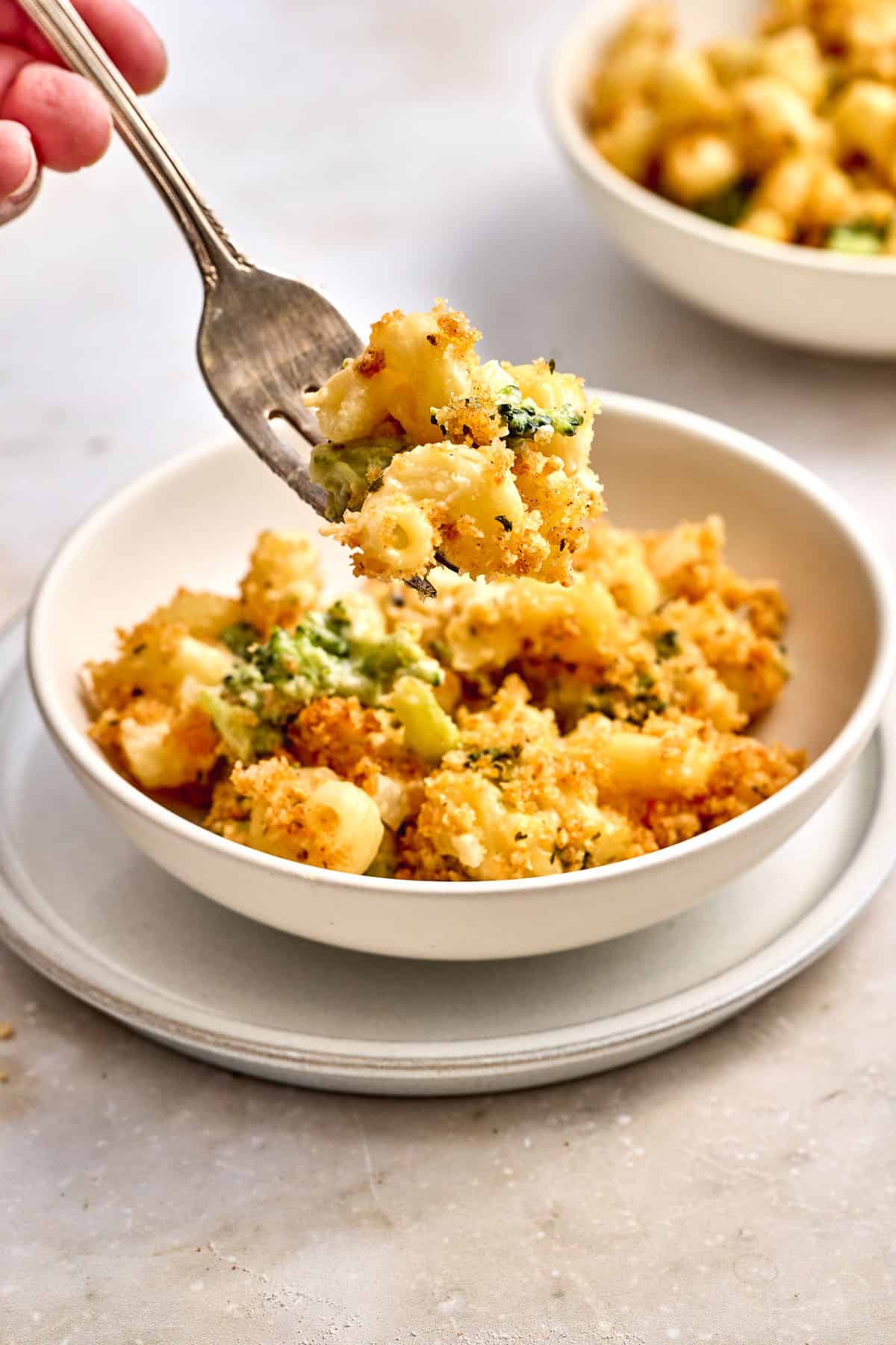 A bowl of baked macaroni and cheese with broccoli, topped with breadcrumbs, with a fork lifting a bite from the bowl.