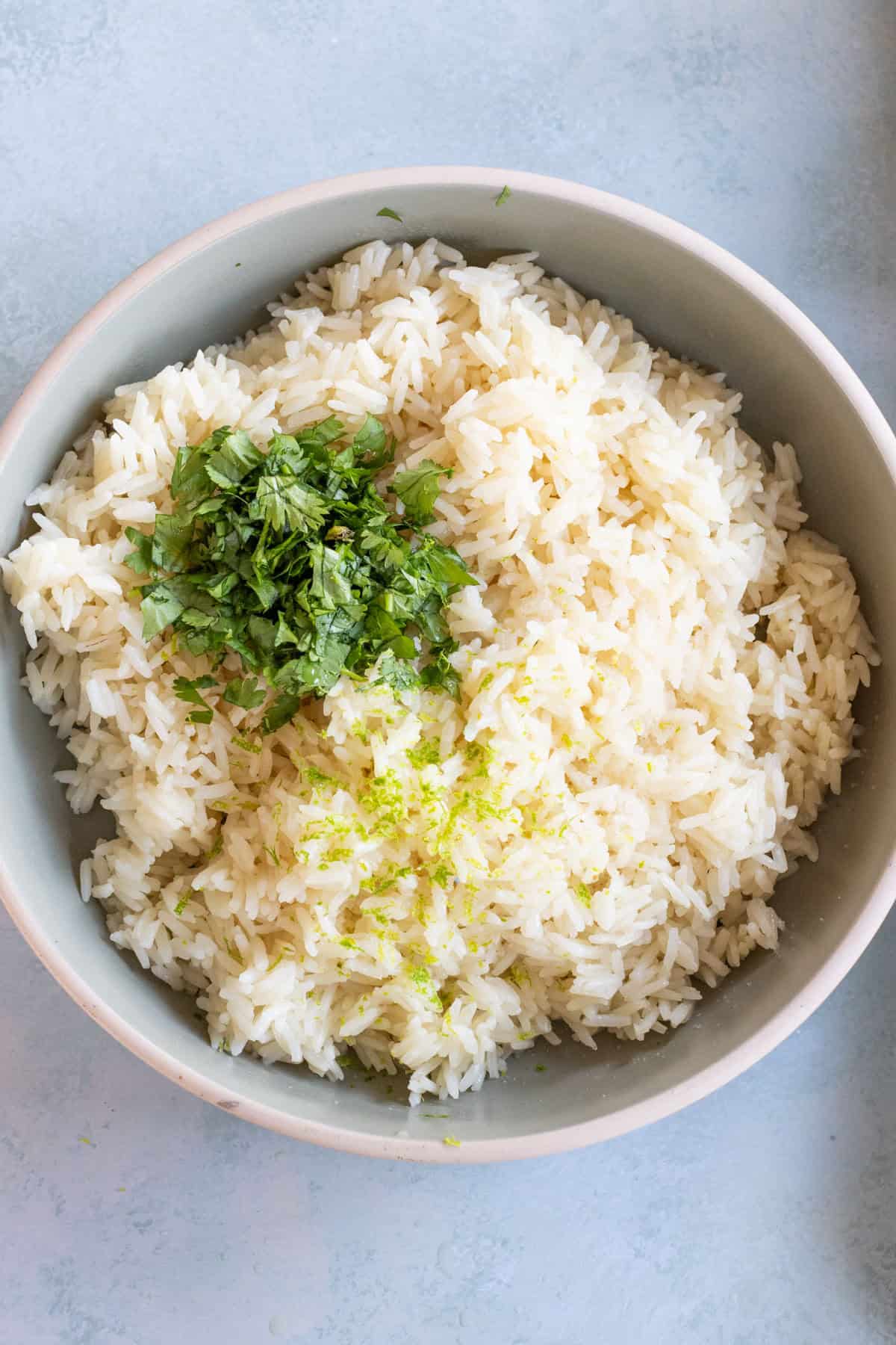 Bowl of fluffy rice topped with chopped fresh herbs and grated lime zest on a light surface.