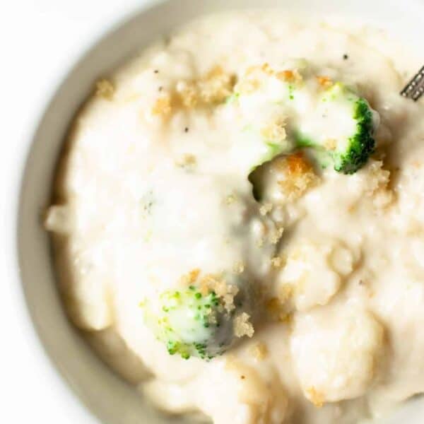 A bowl of creamy white soup with broccoli florets and breadcrumbs, shown close-up.