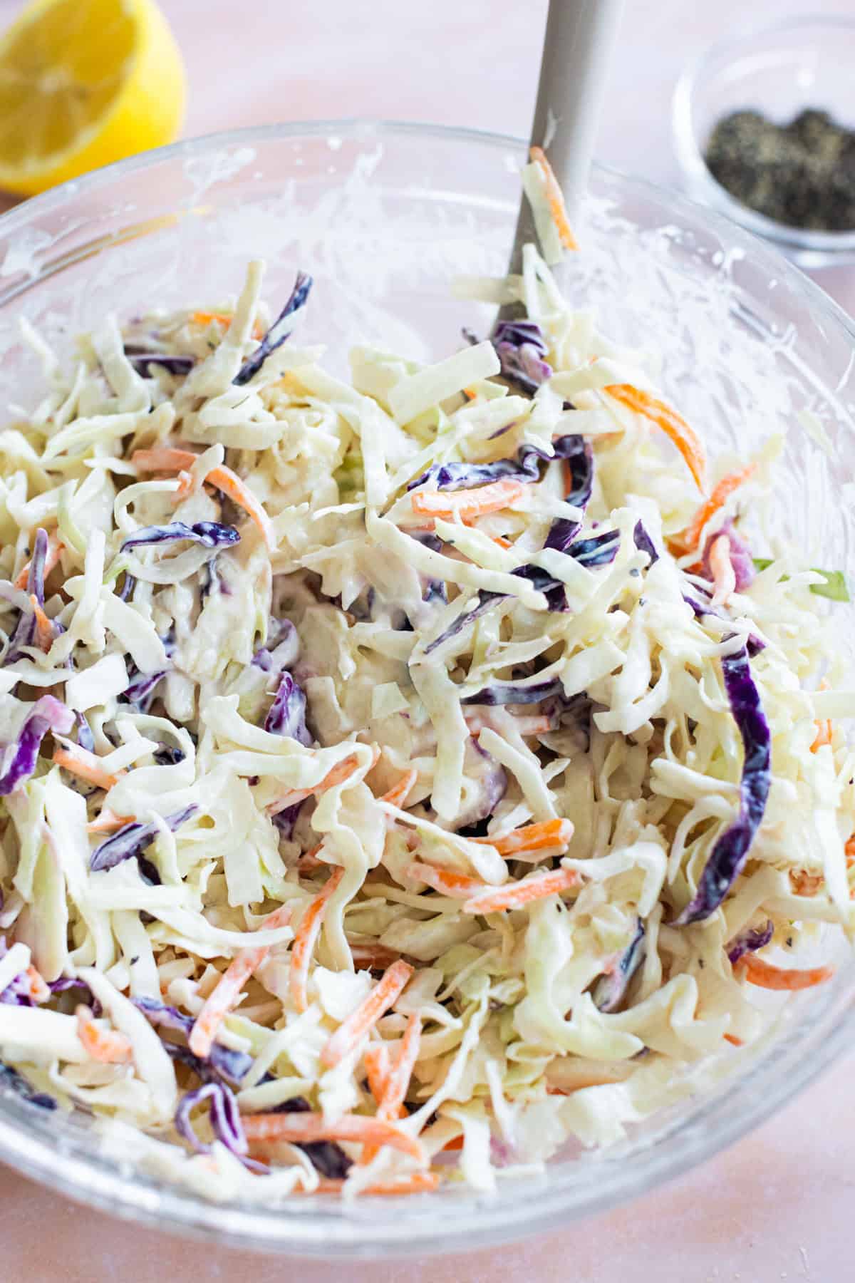 A bowl of coleslaw with shredded cabbage, carrots, and purple cabbage mixed in a creamy dressing, with a spoon inside the bowl.