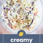 A glass bowl filled with creamy coleslaw containing shredded cabbage, carrots, and purple cabbage, with a serving spoon. Text below reads "creamy coleslaw.