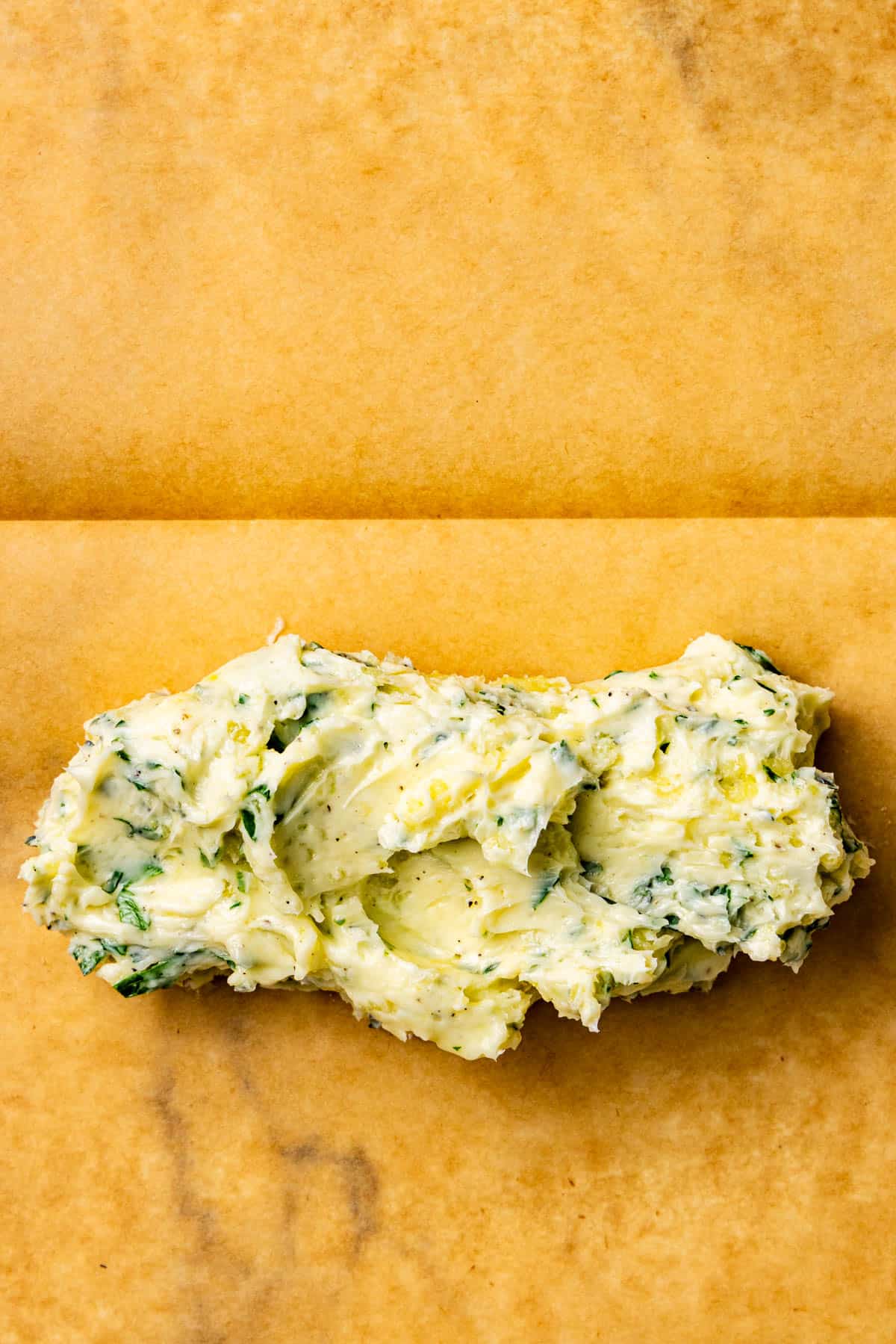 A mound of herbed butter with visible green flecks on a sheet of brown parchment paper.