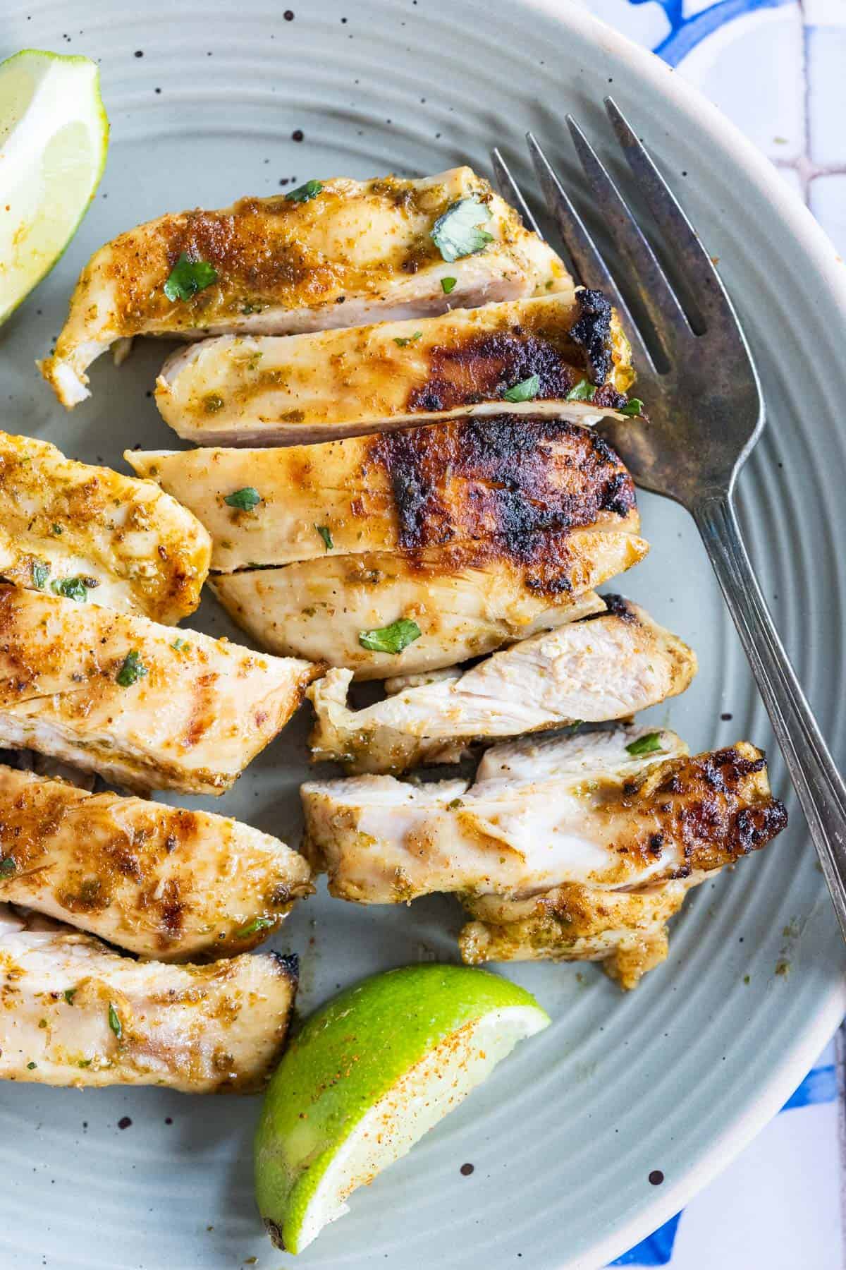 Slices of marinated and grilled chicken breast on a plate with lime wedges and a fork.