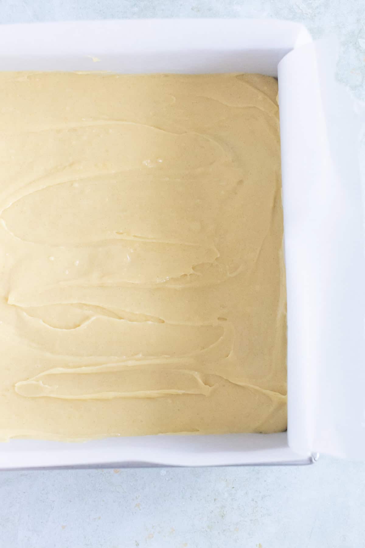 A rectangular baking pan lined with parchment paper is filled with an even layer of light-colored batter, ready to be baked.