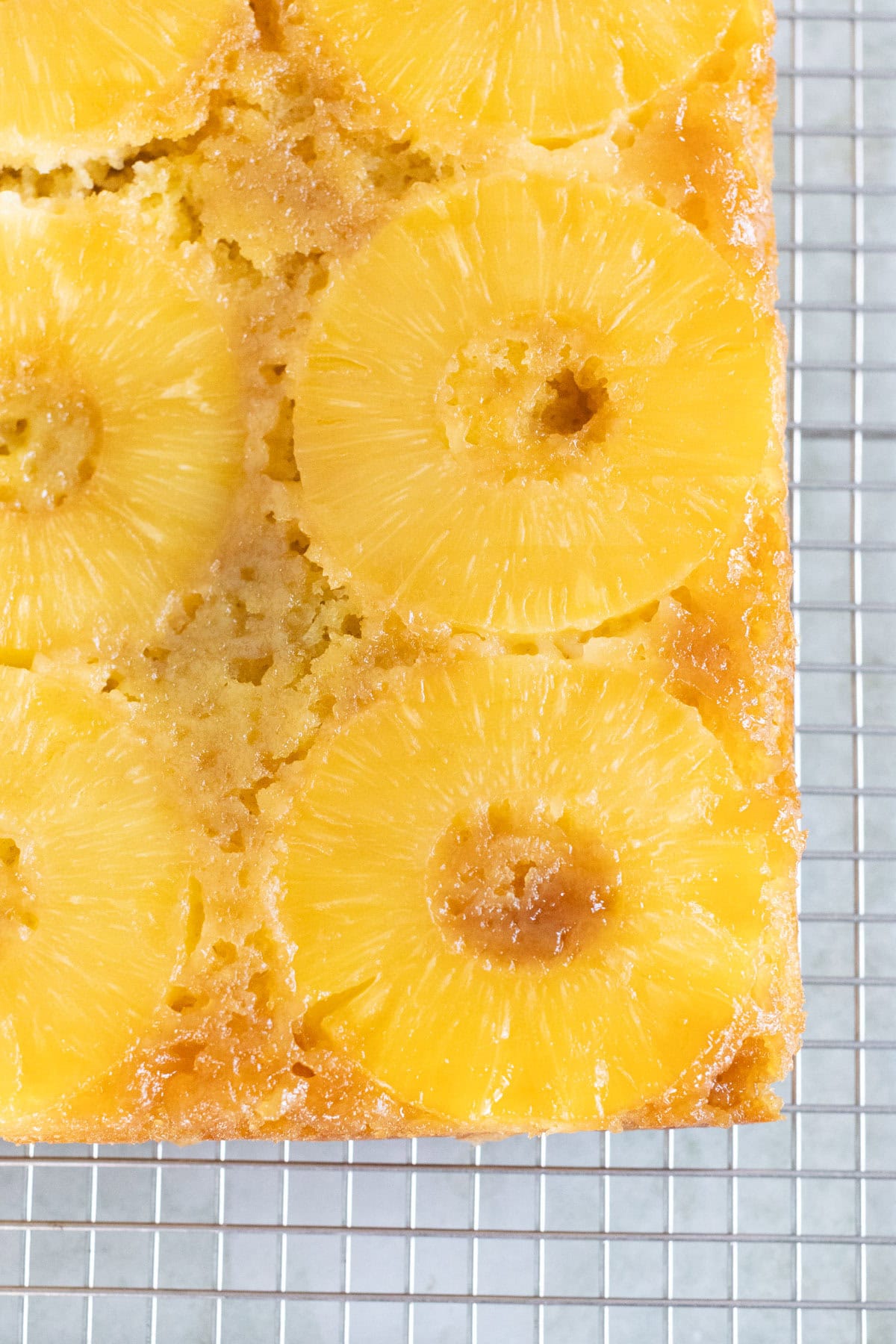 Rectangular pineapple upside-down cake with visible pineapple rings, cooling on a metal wire rack.