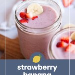 A mason jar filled with pink strawberry banana smoothie, topped with banana slices and chopped strawberries, with another jar and strawberry pieces in the background.