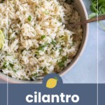 A bowl of cilantro lime rice with a spoon, garnished with fresh cilantro, placed on a light surface.