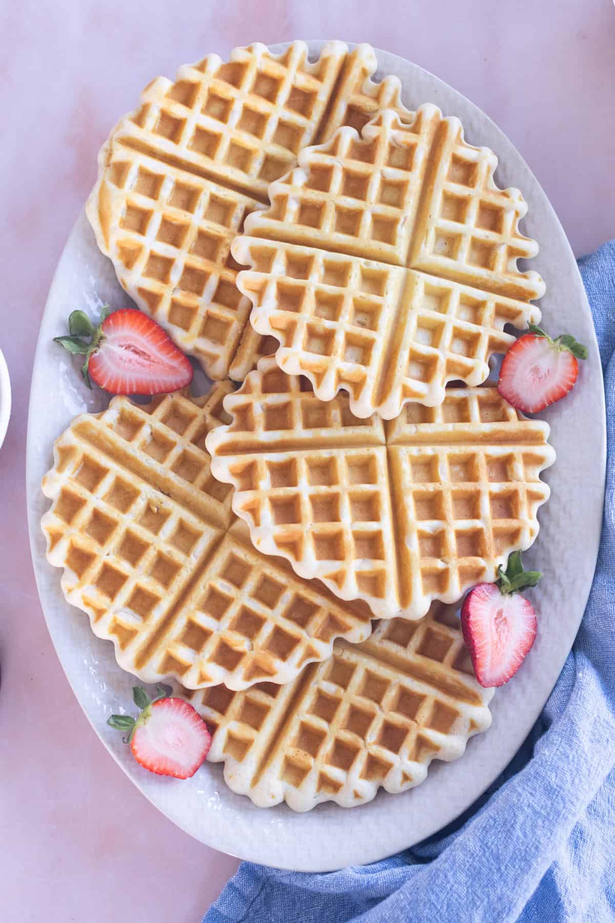 A white platter with five homemade waffles garnished with fresh strawberry slices.