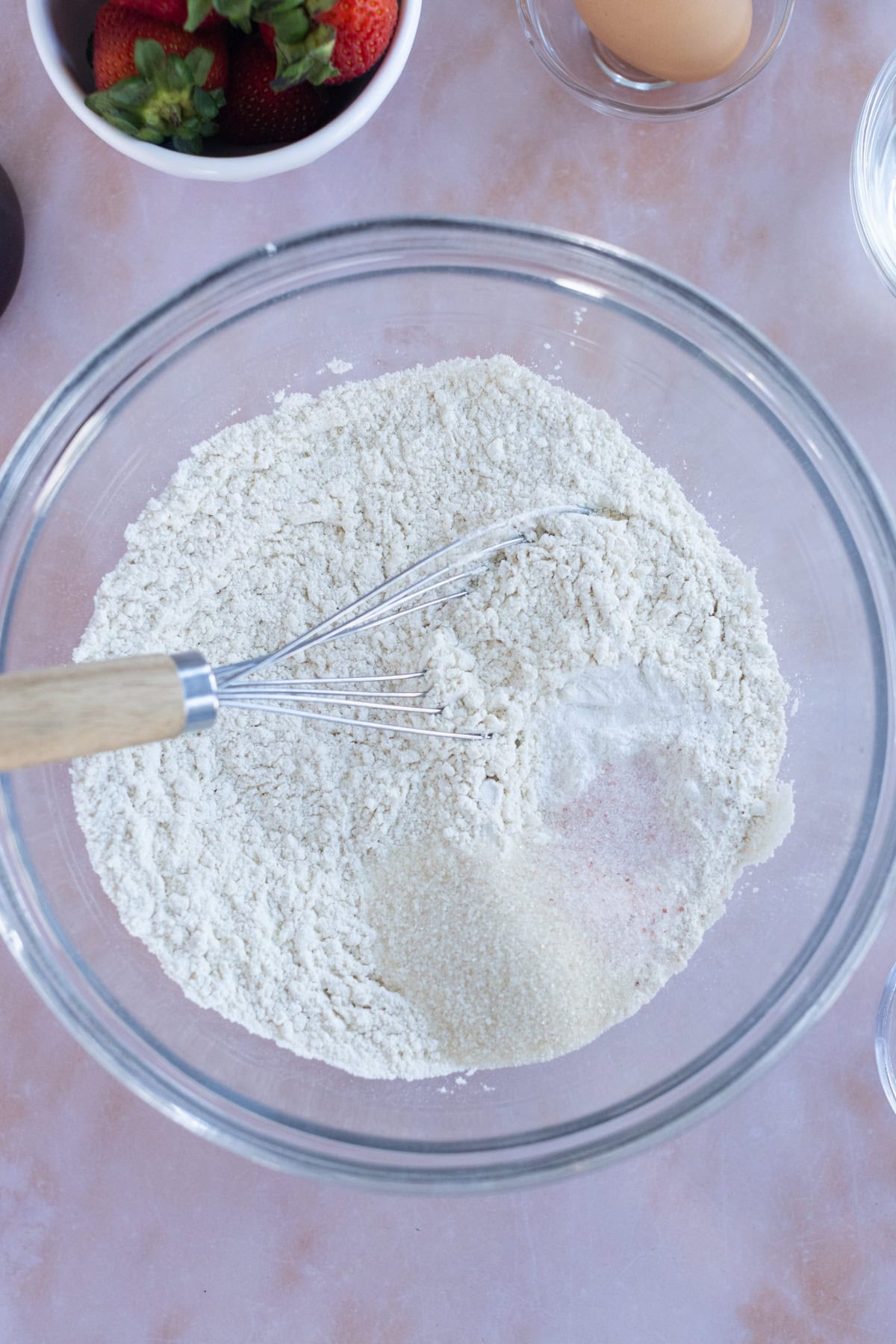 Overhead view of a glass bowl filled with flour and sugar being mixed with a whisk.