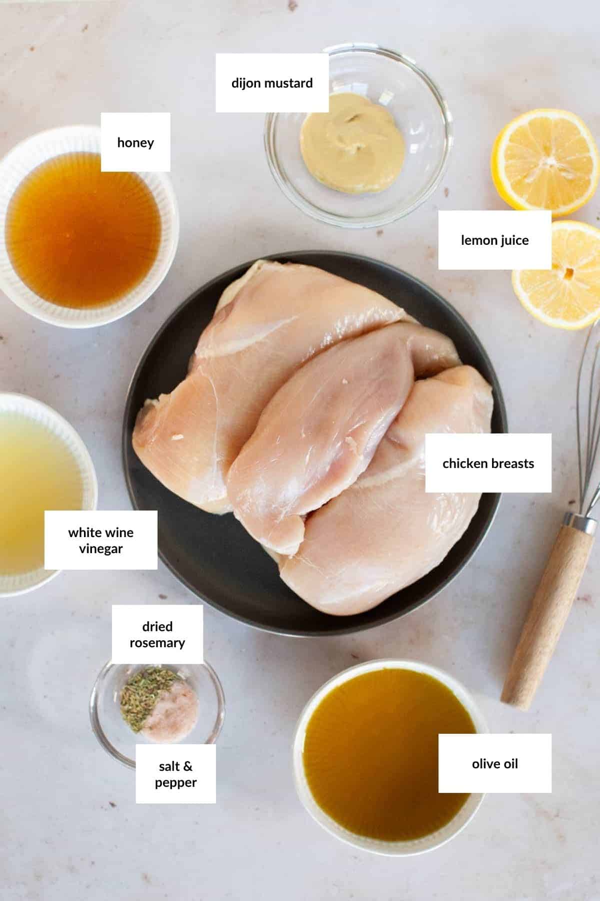 Raw chicken breasts on a plate surrounded by labeled ingredients: honey, white wine vinegar, dried rosemary, salt and pepper, olive oil, lemon juice, and Dijon mustard.
