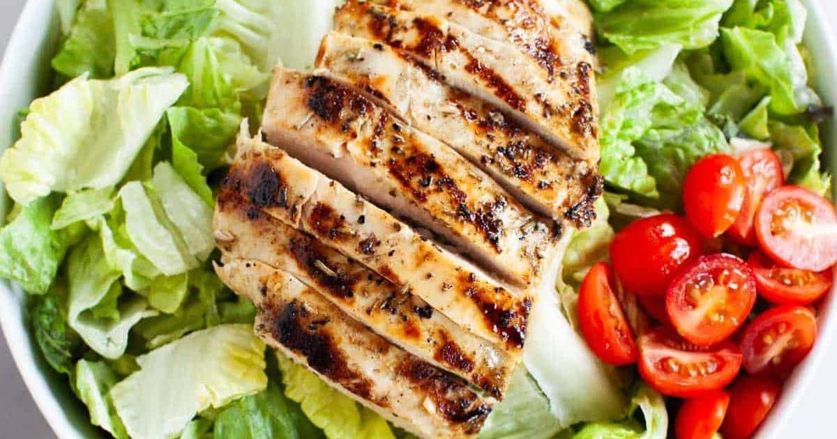 Sliced grilled chicken breast served on a bed of romaine lettuce with halved cherry tomatoes.