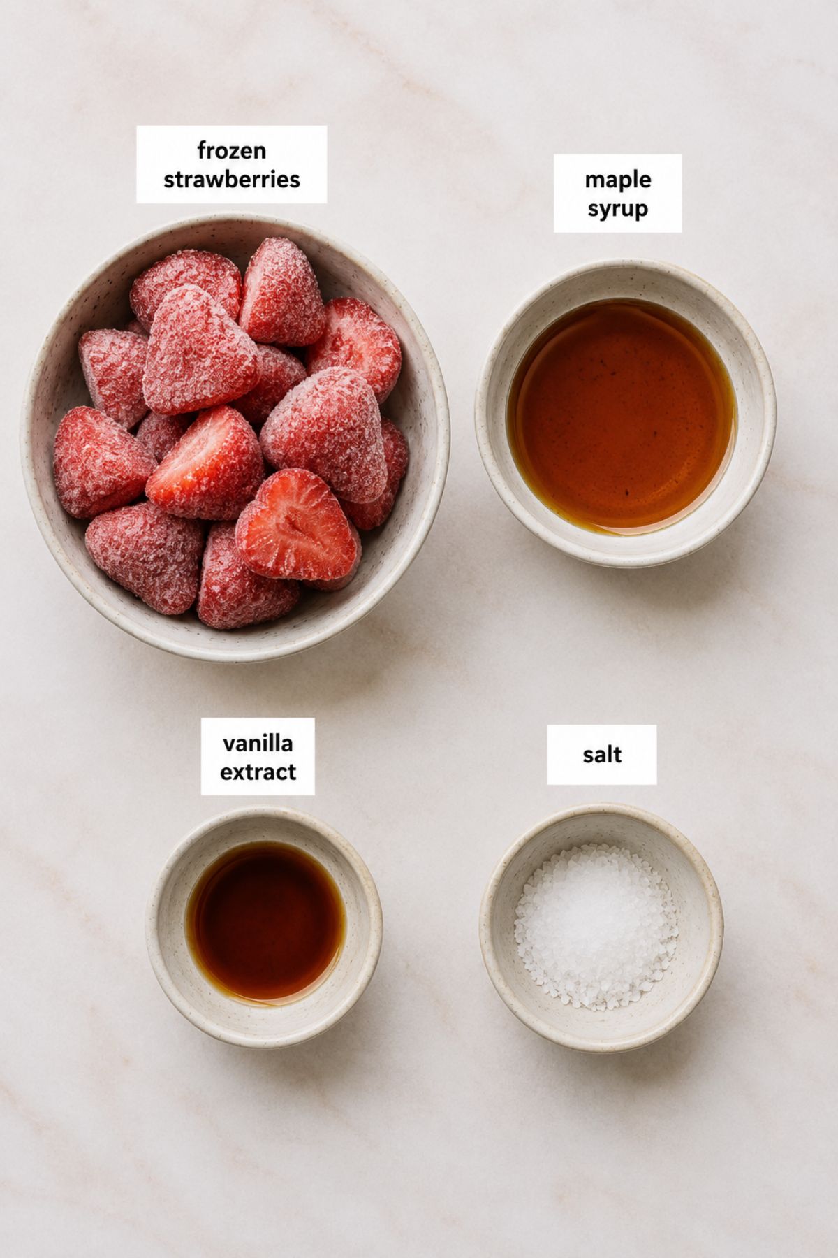 Four bowls on a white surface containing the ingredients for strawberry compote—frozen strawberries, maple syrup, vanilla extract, and salt—each labeled accordingly.