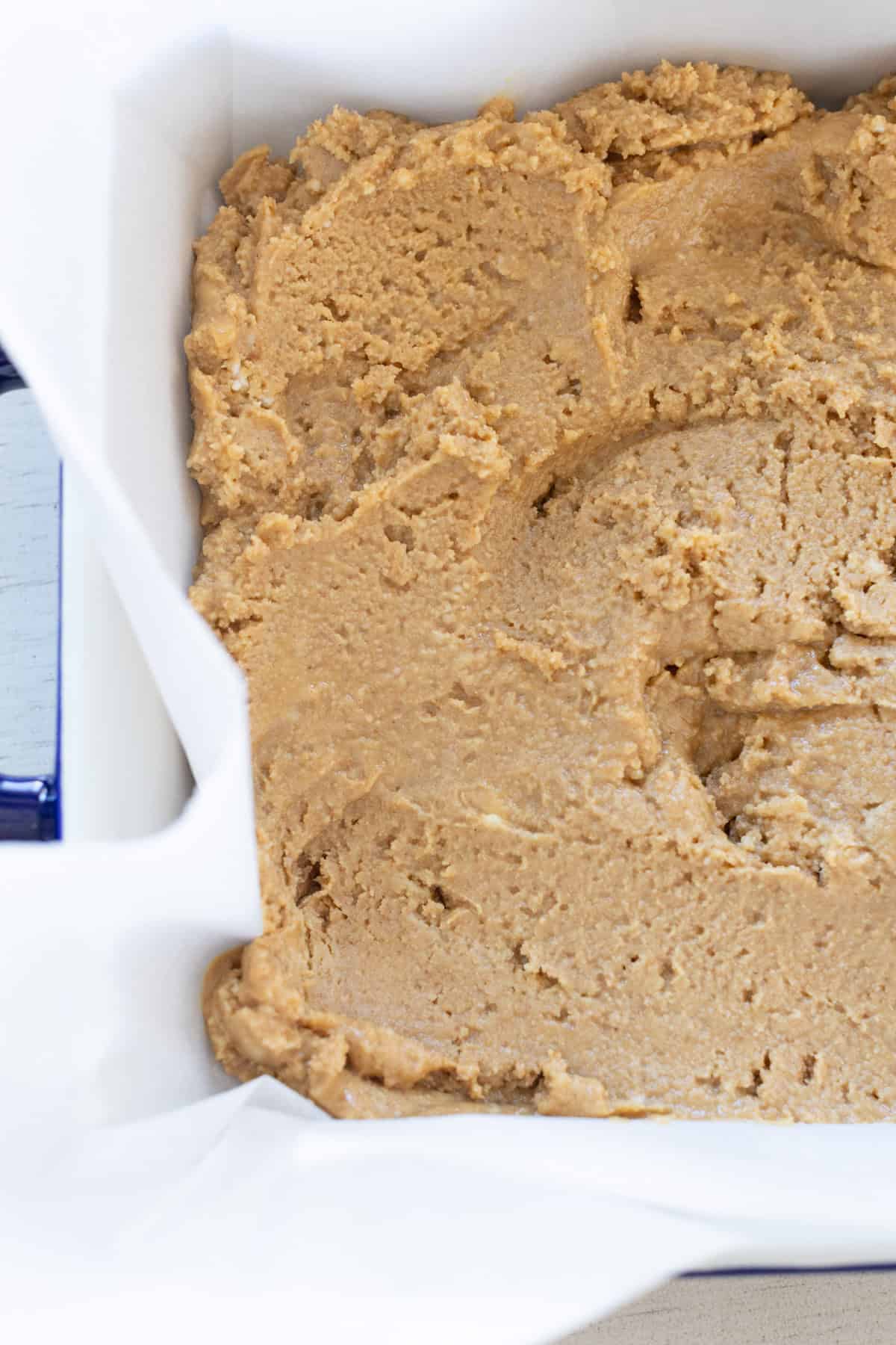 A close-up of unbaked cookie dough spread evenly in a parchment-lined baking dish.