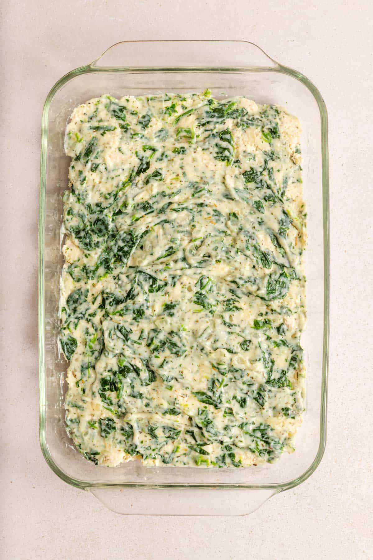 A glass baking dish filled with an uncooked creamy spinach mixture, spread evenly on the bottom.