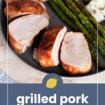 Sliced grilled pork tenderloin served with asparagus and cauliflower on a round plate, seen from above.