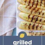 Rectangular slices of grilled squash with beautiful grill marks are arranged on a white plate next to a folded beige cloth. Text overlay reads "grilled squash.