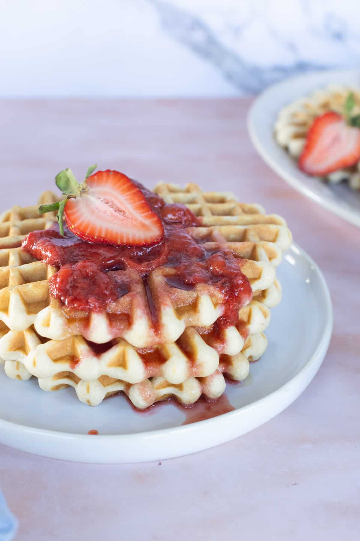 A stack of waffles topped with strawberry sauce and a sliced strawberry, served on a white plate.