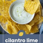 A bowl of cilantro lime crema dip is surrounded by yellow tortilla chips on a plate, with grated lime zest sprinkled on top of the dip.