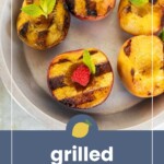 Four grilled peach halves garnished with mint and a raspberry arranged on a round plate, with the text “grilled peaches” on a blue background at the bottom of the image.