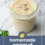 A glass jar filled with creamy homemade chicken soup, topped with cracked black pepper, sits on a marble surface near fresh parsley.