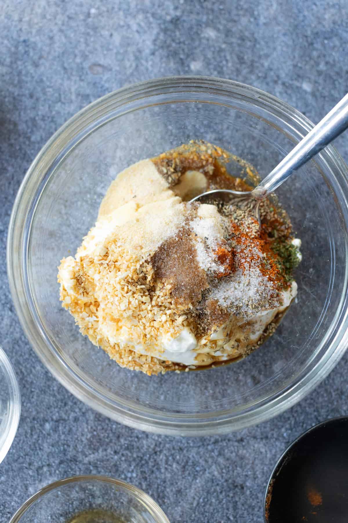Clear glass bowl with various spices, seasonings, and sour cream.