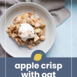 A plate of apple crisp topped with a scoop of ice cream is on a light cloth, next to a baking dish of more apple crisp.