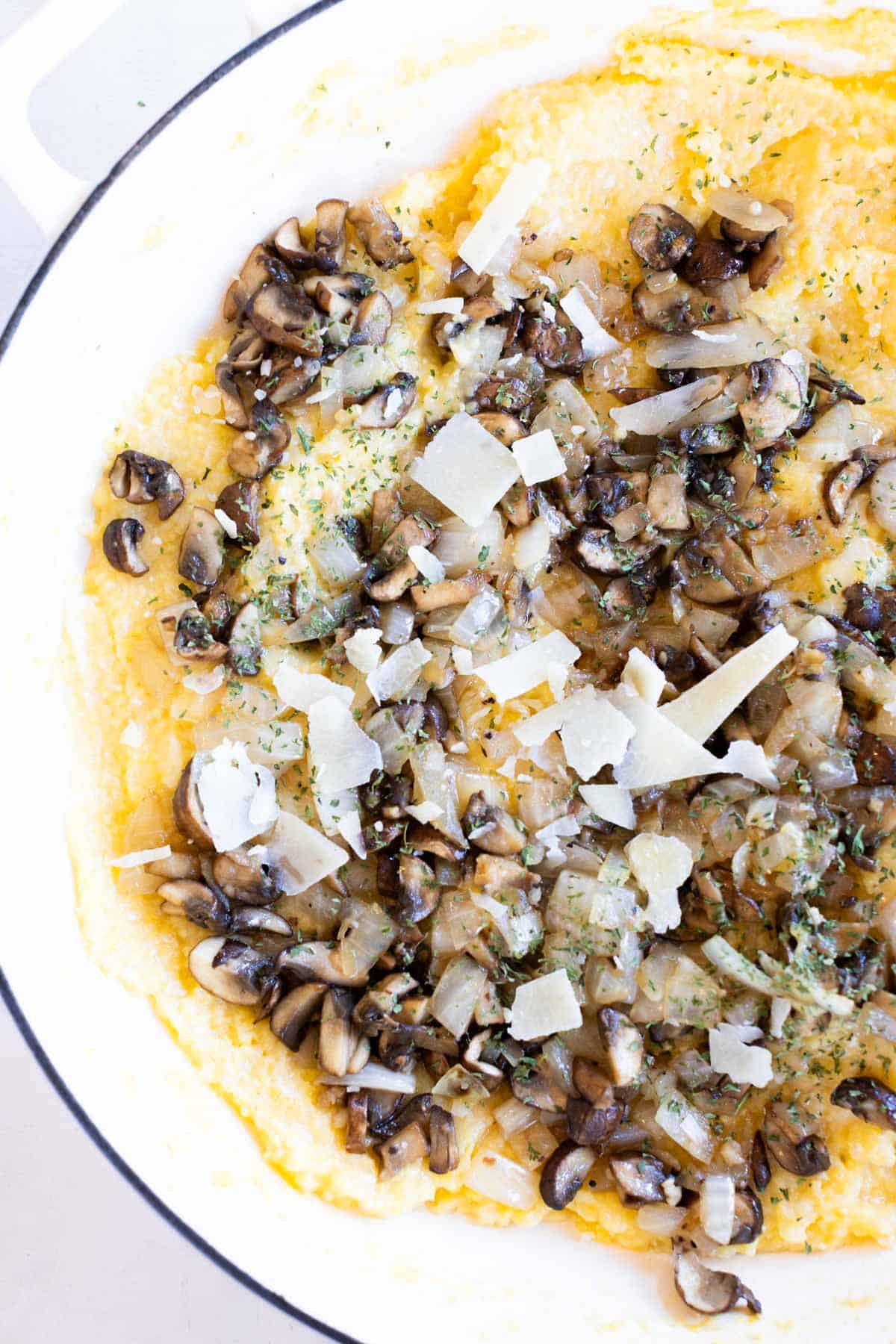 Parmesan polenta topped with sautéed mushrooms, chopped onions, parsley, and shaved parmesan cheese in a white dish.
