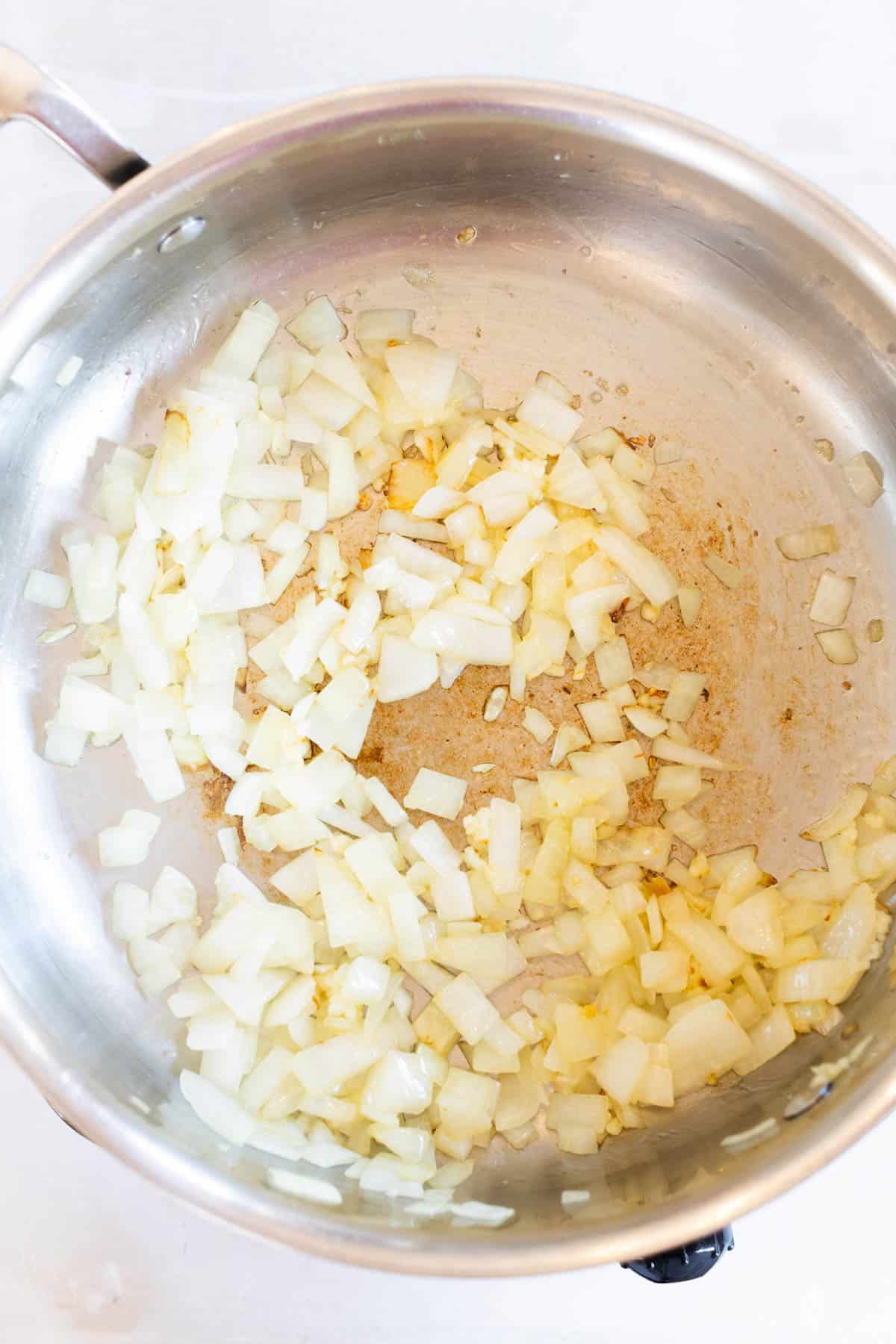 Diced shallot sautéing in a stainless steel pot, turning translucent with some browning on the bottom of the pan.