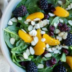 Spinach salad topped with mandarin orange segments, fresh blackberries, dried cranberries, crumbled cheese, and sliced almonds.