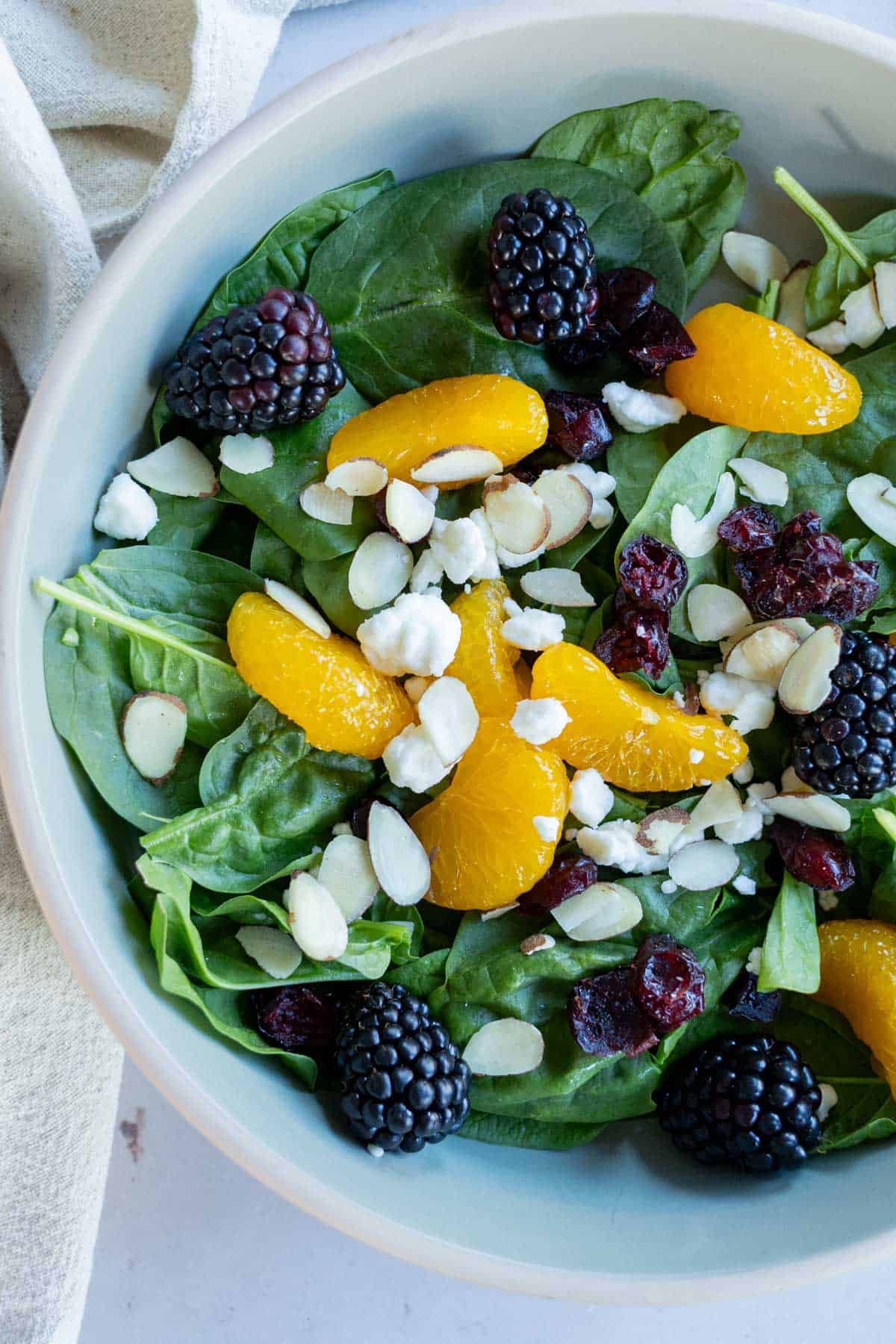 Spinach salad topped with mandarin orange segments, fresh blackberries, dried cranberries, crumbled cheese, and sliced almonds.