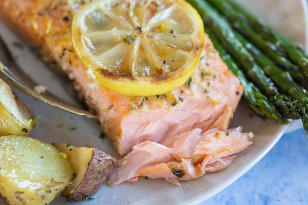 A cooked salmon fillet topped with a lemon slice, served with roasted potatoes and asparagus.