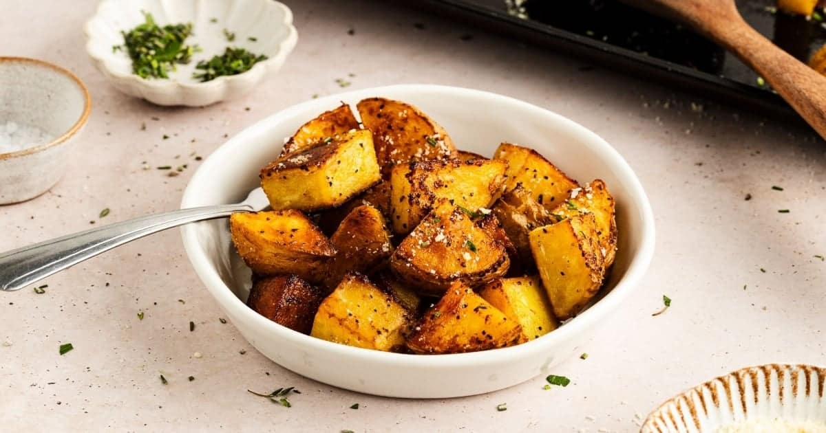 A bowl of roasted potato wedges garnished with herbs.