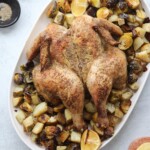 Roast spatchcock chicken on a platter with roasted potatoes, Brussels sprouts, chopped lemons, and seasoning bowls nearby.